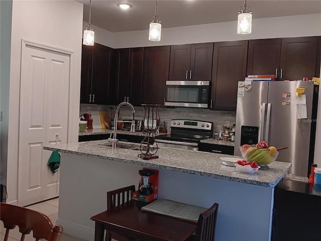 kitchen with stainless steel appliances, decorative backsplash, light stone countertops, pendant lighting, and dark brown cabinetry