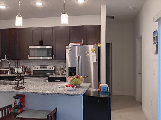 kitchen with light tile patterned floors, stainless steel appliances, hanging light fixtures, light stone counters, and dark brown cabinetry