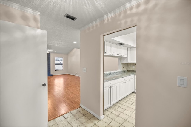 hallway with a textured ceiling, light tile patterned floors, and crown molding