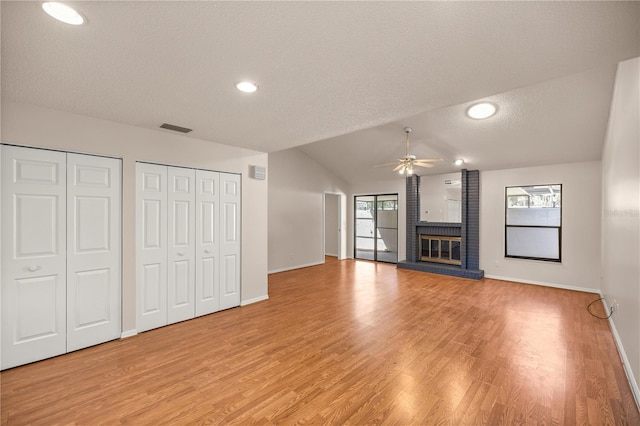 unfurnished living room with a textured ceiling, vaulted ceiling, a fireplace, ceiling fan, and wood-type flooring