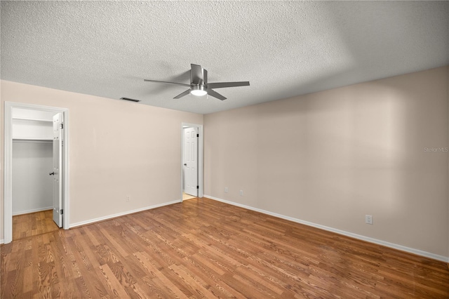 unfurnished bedroom with a textured ceiling, a spacious closet, a closet, hardwood / wood-style floors, and ceiling fan