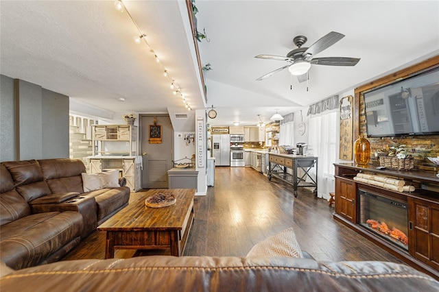 living area featuring dark wood-type flooring, a textured ceiling, a glass covered fireplace, lofted ceiling, and ceiling fan