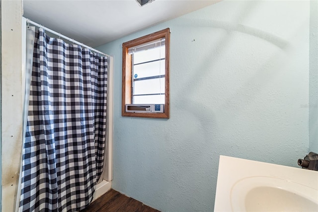 full bath with curtained shower, wood finished floors, and a textured wall