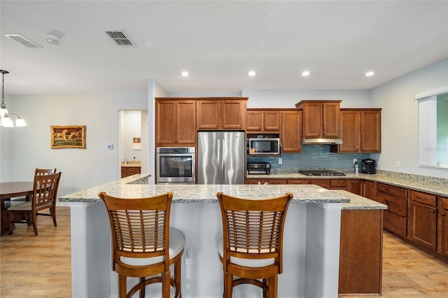 kitchen with a kitchen breakfast bar, backsplash, light hardwood / wood-style floors, decorative light fixtures, and appliances with stainless steel finishes