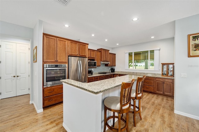 kitchen featuring a kitchen bar, light wood-type flooring, light stone counters, stainless steel appliances, and a center island