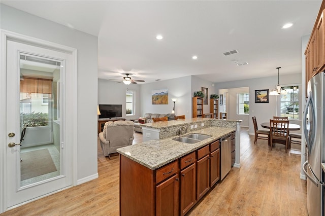 kitchen featuring light stone countertops, stainless steel appliances, a kitchen island with sink, sink, and hanging light fixtures