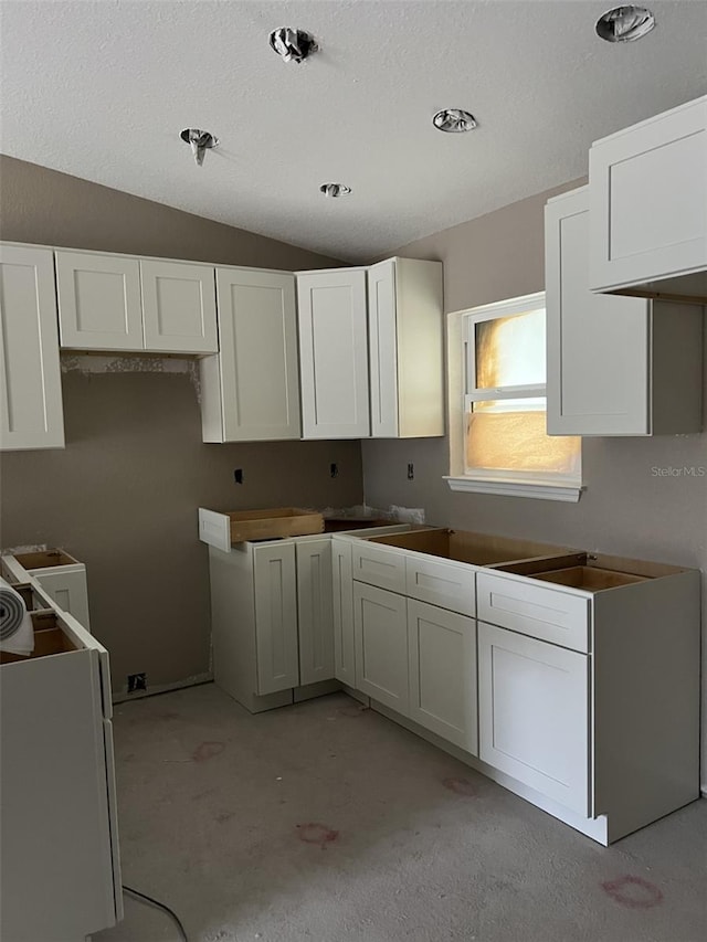 kitchen featuring a textured ceiling, washer / clothes dryer, white cabinetry, and vaulted ceiling