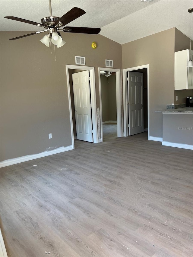 interior space featuring ceiling fan, vaulted ceiling, a textured ceiling, and light wood-type flooring