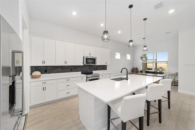 kitchen with a center island with sink, appliances with stainless steel finishes, white cabinetry, and sink