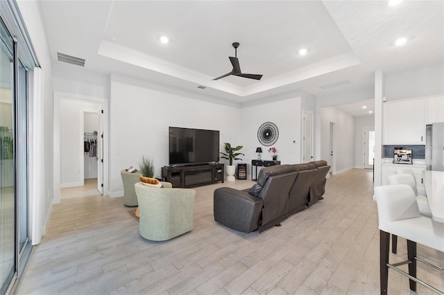 living room featuring ceiling fan, crown molding, light hardwood / wood-style flooring, and a raised ceiling