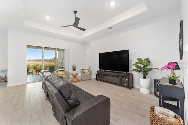 living room with ceiling fan, ornamental molding, light hardwood / wood-style floors, and a tray ceiling