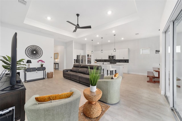 living room featuring ceiling fan, light hardwood / wood-style flooring, and a tray ceiling