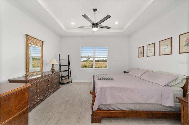 bedroom featuring ceiling fan, a raised ceiling, and light hardwood / wood-style flooring