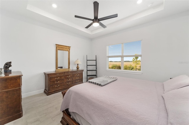 bedroom with ceiling fan, a tray ceiling, and light hardwood / wood-style flooring