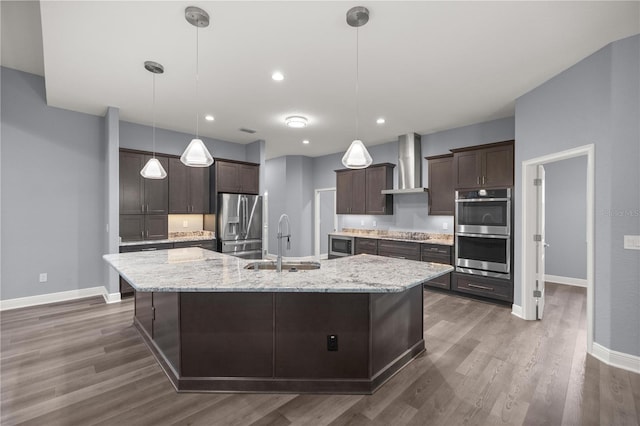 kitchen with a spacious island, wall chimney range hood, sink, decorative light fixtures, and stainless steel appliances