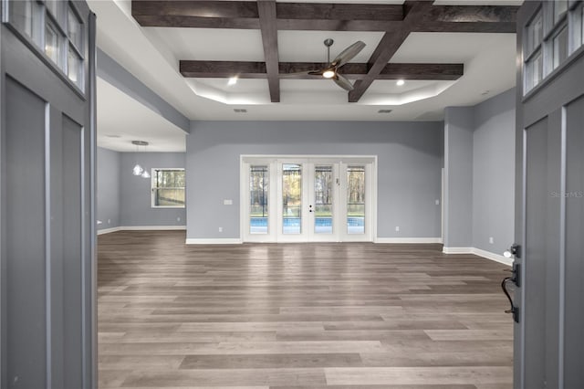 unfurnished living room featuring beam ceiling, coffered ceiling, light hardwood / wood-style floors, and ceiling fan with notable chandelier