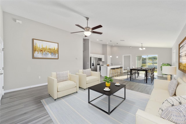 living room featuring light wood-type flooring, vaulted ceiling, and ceiling fan with notable chandelier