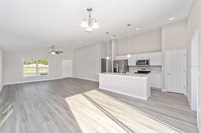 kitchen with ceiling fan with notable chandelier, white cabinets, stainless steel appliances, hanging light fixtures, and a kitchen island with sink