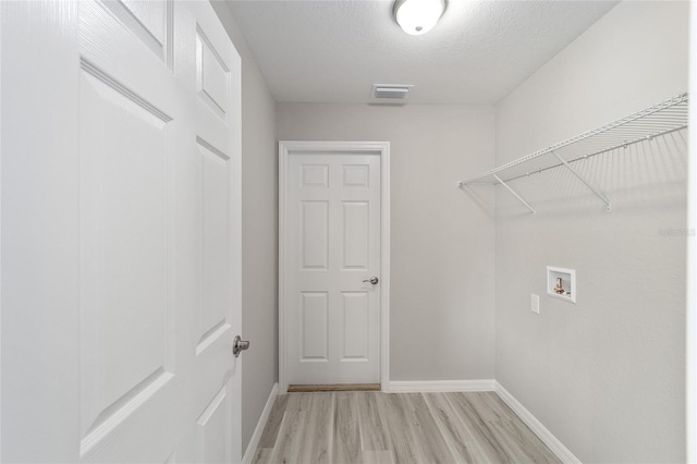 washroom with a textured ceiling, light hardwood / wood-style floors, and hookup for a washing machine