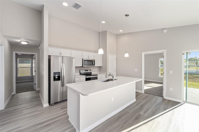 kitchen with decorative light fixtures, white cabinetry, stainless steel appliances, an island with sink, and sink