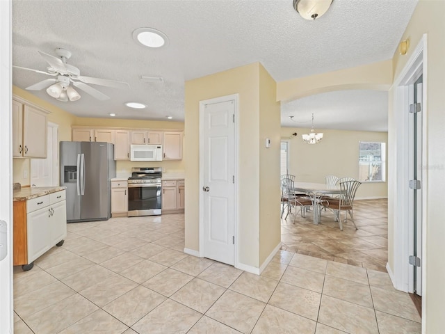 kitchen with light tile patterned floors, arched walkways, ceiling fan with notable chandelier, light countertops, and appliances with stainless steel finishes