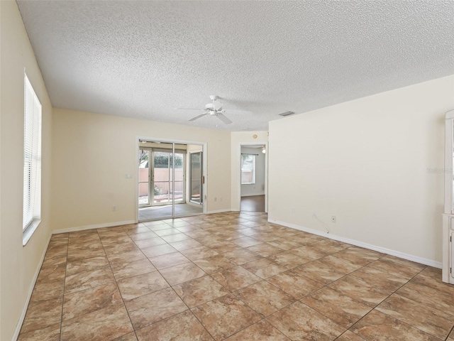 empty room with ceiling fan, a textured ceiling, baseboards, and light tile patterned floors