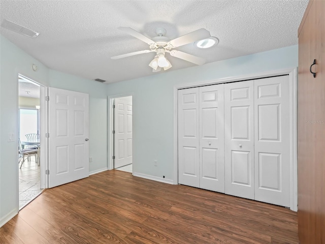 unfurnished bedroom featuring a closet, visible vents, a textured ceiling, and wood finished floors