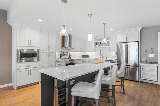 kitchen featuring appliances with stainless steel finishes, wall chimney exhaust hood, sink, white cabinetry, and a kitchen island