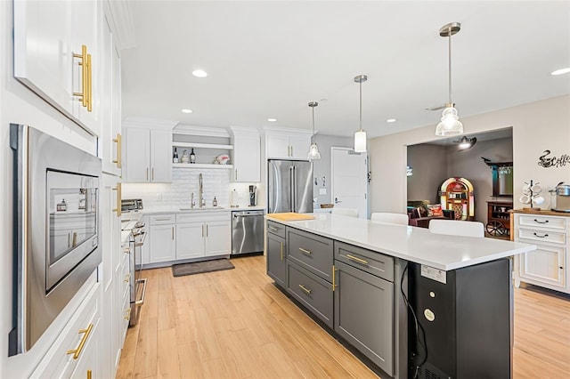 kitchen with appliances with stainless steel finishes, a kitchen island, sink, pendant lighting, and white cabinetry