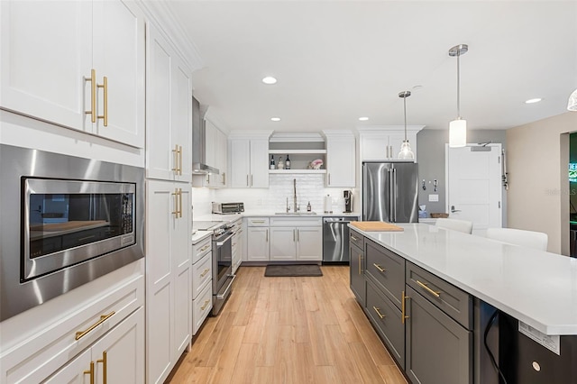 kitchen featuring white cabinetry, sink, wall chimney exhaust hood, hanging light fixtures, and appliances with stainless steel finishes