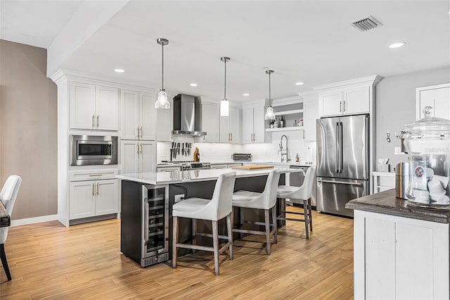 kitchen with white cabinetry, wall chimney exhaust hood, stainless steel appliances, and a kitchen island