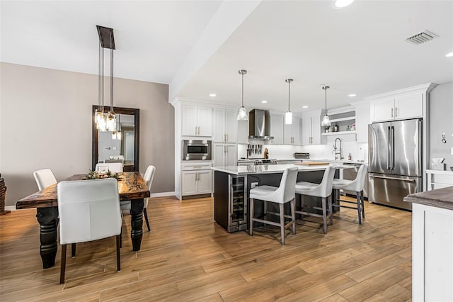 kitchen featuring appliances with stainless steel finishes, wall chimney range hood, pendant lighting, light hardwood / wood-style floors, and white cabinetry