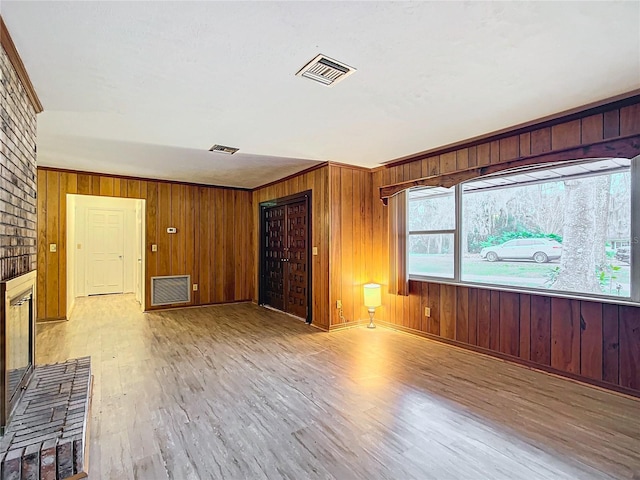 empty room with light hardwood / wood-style floors, crown molding, and wooden walls