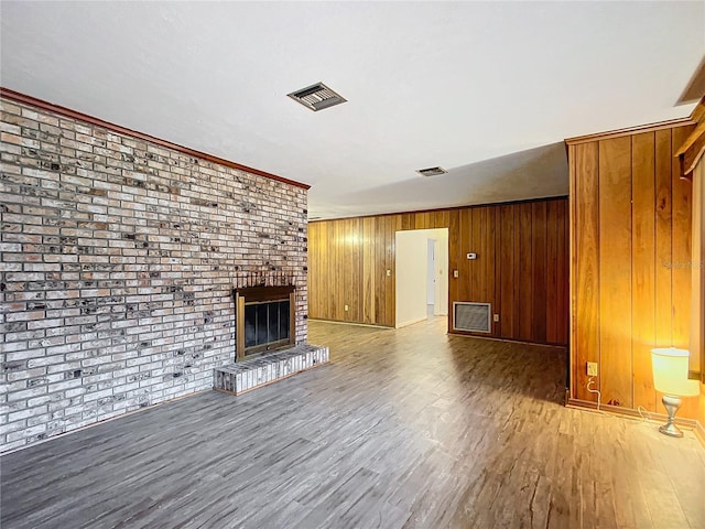 unfurnished living room featuring a fireplace, ornamental molding, hardwood / wood-style flooring, wood walls, and brick wall