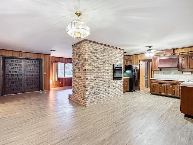 kitchen featuring black appliances, light hardwood / wood-style floors, brick wall, custom range hood, and decorative light fixtures