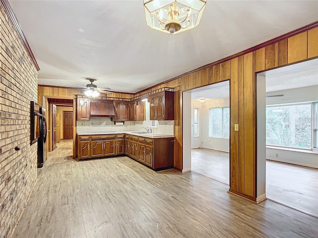 kitchen with sink, refrigerator, light wood-type flooring, ceiling fan with notable chandelier, and brick wall