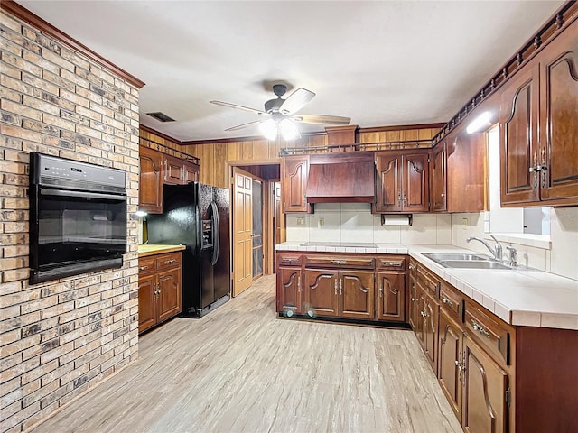 kitchen with custom exhaust hood, light hardwood / wood-style floors, black appliances, ceiling fan, and sink