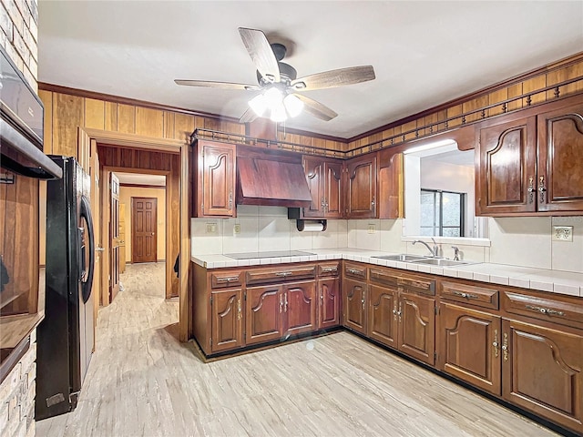 kitchen featuring sink, light wood-type flooring, tile counters, premium range hood, and black appliances