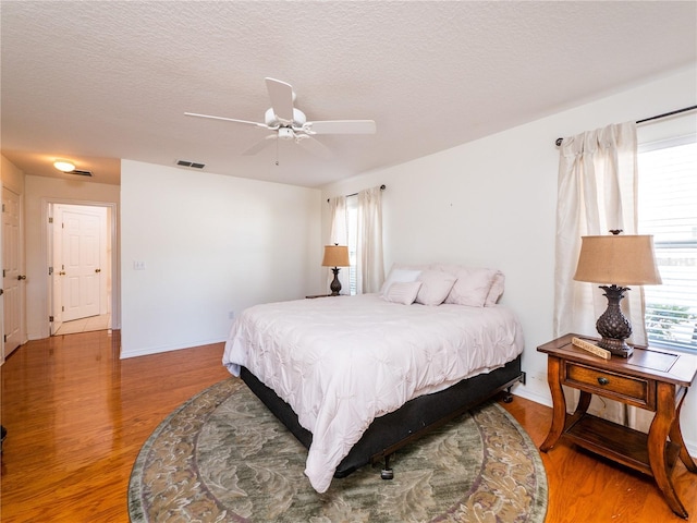 bedroom featuring ceiling fan, wood-type flooring, multiple windows, and a textured ceiling