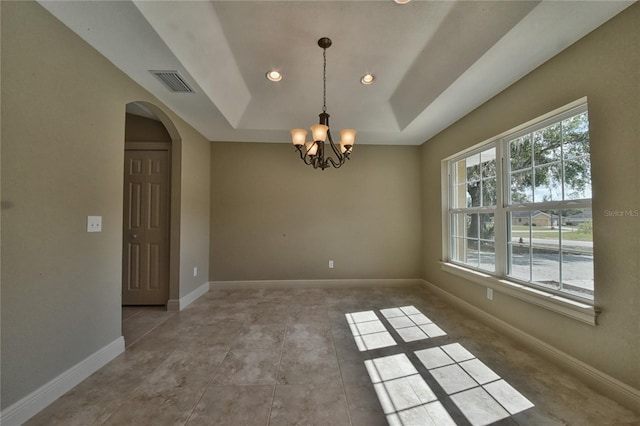 tiled empty room featuring a chandelier and a tray ceiling