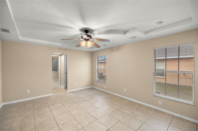 tiled empty room with a tray ceiling, ceiling fan, and a textured ceiling