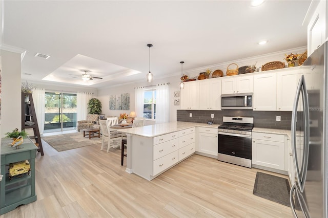 kitchen with decorative light fixtures, a raised ceiling, kitchen peninsula, stainless steel appliances, and white cabinets