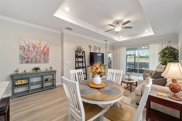 dining room with ceiling fan, a tray ceiling, light hardwood / wood-style flooring, and crown molding