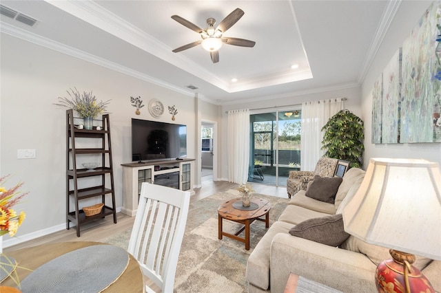 living room featuring ceiling fan, light hardwood / wood-style floors, ornamental molding, and a raised ceiling