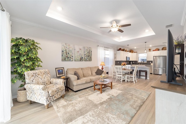 living room featuring a raised ceiling, ceiling fan, crown molding, and light hardwood / wood-style floors