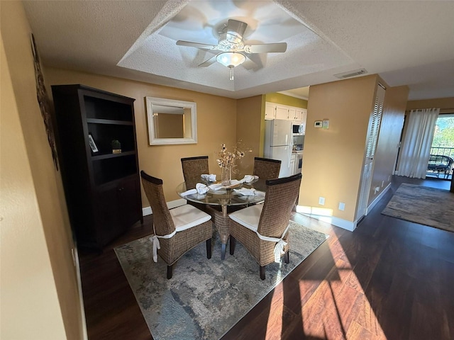 dining room with dark hardwood / wood-style flooring, ceiling fan, a raised ceiling, and a textured ceiling