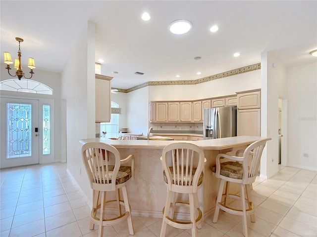 kitchen with kitchen peninsula, an inviting chandelier, stainless steel fridge with ice dispenser, light tile patterned floors, and light brown cabinetry