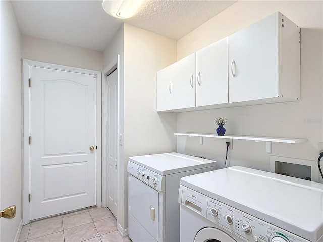 laundry room featuring light tile patterned floors, washing machine and dryer, a textured ceiling, and cabinets