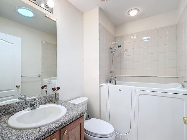 bathroom with toilet, vanity, and washer / dryer