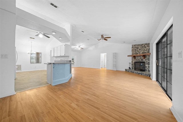 unfurnished living room featuring vaulted ceiling, light hardwood / wood-style floors, a stone fireplace, and a notable chandelier